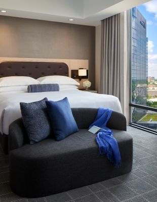 A king bed with white linens and a sitting bench at the end of the bed with blue pillows