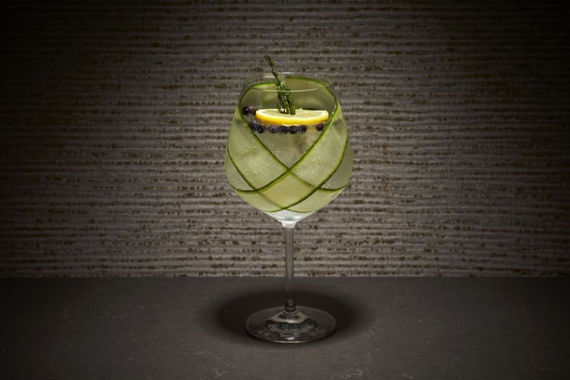 Cocktail in a wine glass with cucumber and lemon garnish