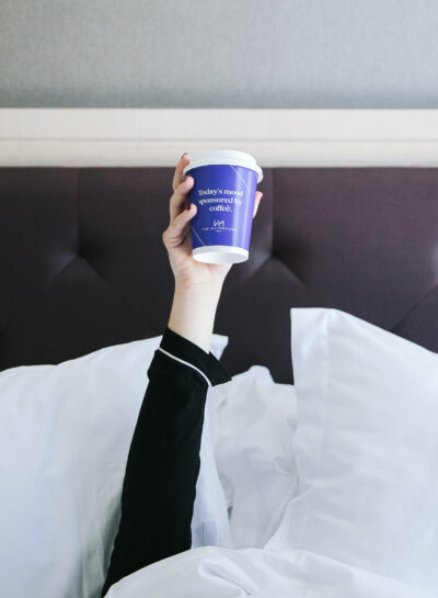 A Person in bed holding a blue cup up in the air from the room of The Watermark Hotel